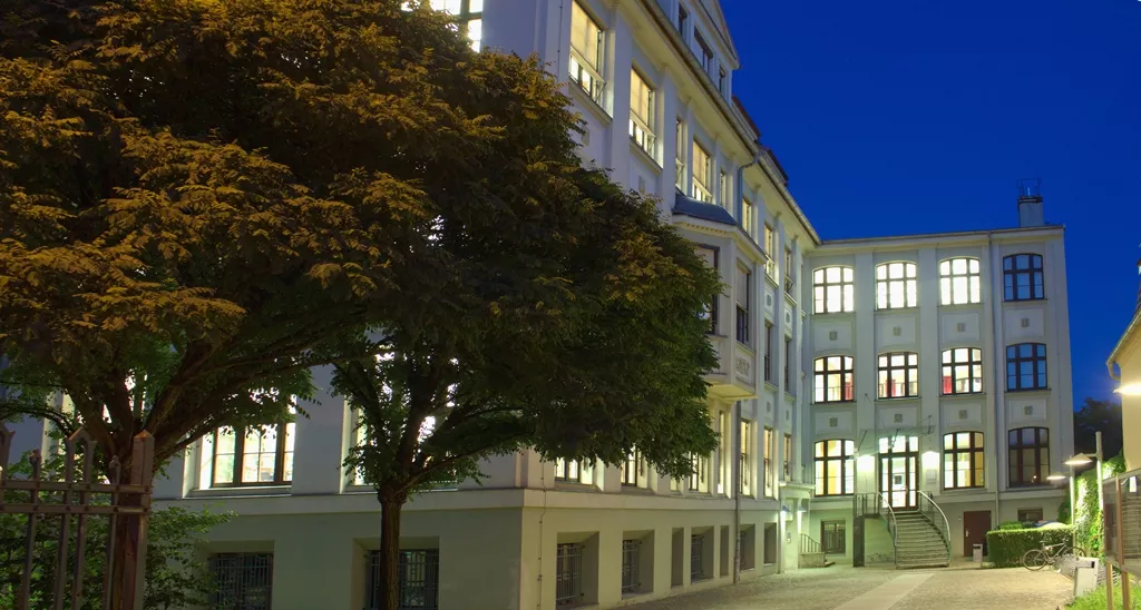 Auf dem Foto sieht man das Gebäude Berliner Straße 13/14. Es ist Abend. Alle Fenster sind erleuchtet.